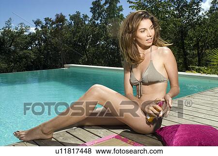 Woman sitting on a wood deck by a swimming pool with sunscreen View Large Photo Image Stock Photo - Woman sitting on a wood deck by a swimming pool with sunscreen. Fotosearch