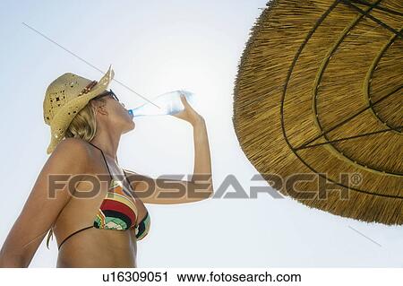 Woman standing near a beach umbrella drinking a bottle of water. View Large Photo Image Stock Image - Woman standing near a beach umbrella drinking a bottle of water.. Fotosearch