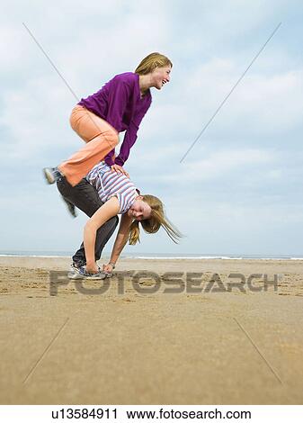 Stock Image - Two females playing leap-frog on beach. Fotosearch