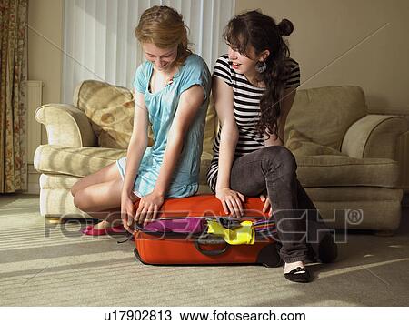 Stock Image - Two females trying to close suitcase. Fotosearch