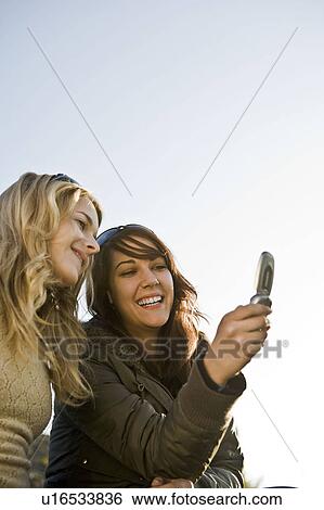 Stock Photograph - Two girls looking at mobile together. Fotosearch