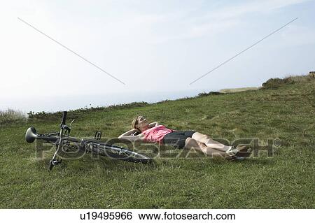 A woman rests on grass by her Bicycle. View Large Photo Image Stock Photograph - A woman rests on grass by her Bicycle.. Fotosearch