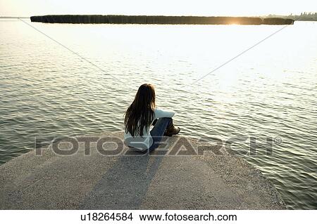 Picture - Girl sitting by lake.. Fotosearch
