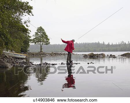 Woman balancing on rocks in the water near a boat. View Large Photo Image Stock Photograph - Woman balancing on rocks in the water near a boat.. Fotosearch
