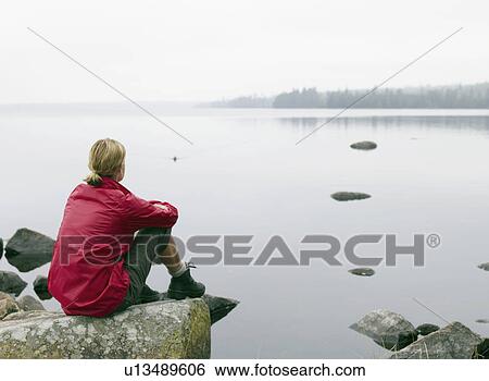 Woman sitting on large rocks by a lake. View Large Photo Image Stock Photograph - Woman sitting on large rocks by a lake.. Fotosearch