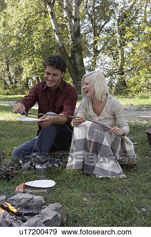 Couple At Campsite Cooking Hotdogs Over The Fire Pit Stock Photo