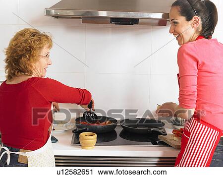 Stock Image - Mature mother and young daughter cooking together, rear view. Fotosearch
