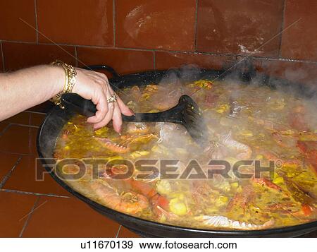 Stock Photo - Person stirring seafood paella, close-up. Fotosearch