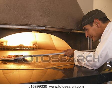 Stock Image - Pizza chef placing pizza in oven. Fotosearch