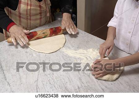 Stock Photo - Senior woman and girl (9-11) rolling pastry, close-up. Fotosearch