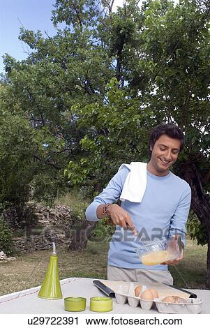 Stock Image - Young man beating eggs. Fotosearch