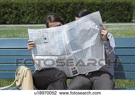 Businessman and woman on bench in park reading a newspaper together hiding behind. View Large Photo Image Stock Image - Businessman and woman on bench in park reading a newspaper together hiding behind.. Fotosearch