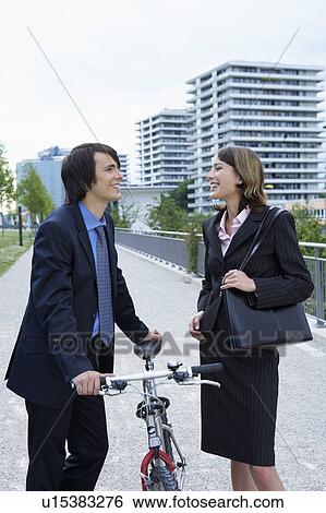 Stock Photograph - Businessman and woman talking in-between bike laughing.. Fotosearch