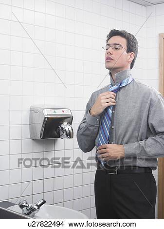 Man reflected in office washroom mirror doing up his tie View Large Photo Image Picture - Man reflected in office washroom mirror doing up his tie. Fotosearch