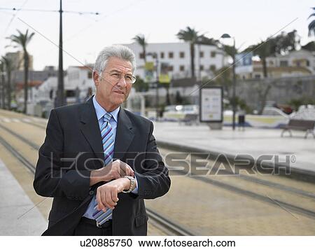 Senior businessman checking watch waiting by tramway View Large Photo Image Stock Image - Senior businessman checking watch waiting by tramway. Fotosearch