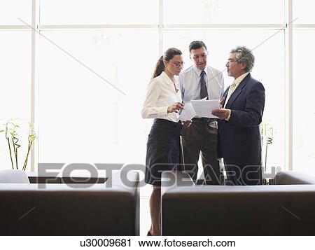 Stock Image - Two businessmen and woman discussing file in office. Fotosearch