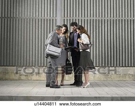 Stock Image - Two businesswomen and two businessmen looking at paper by concrete wall, Alicante, Spain,. Fotosearch