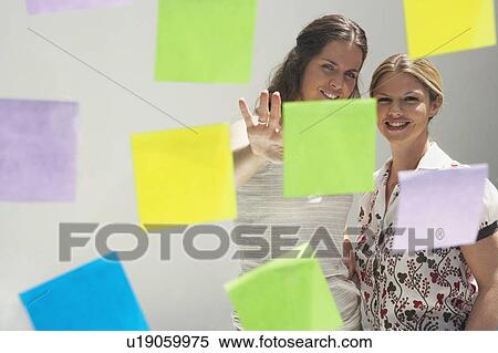 Stock Photography - Two young women seen through window with colored swatches / PostIt Notes.. Fotosearch