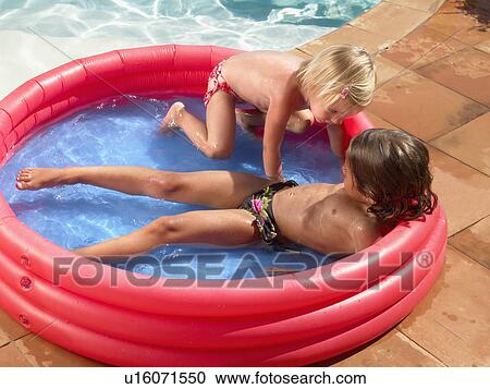 Two children playing in a kiddie pool by a backyard pool. View Large Photo Image Stock Image - Two children playing in a kiddie pool by a backyard pool.. Fotosearch