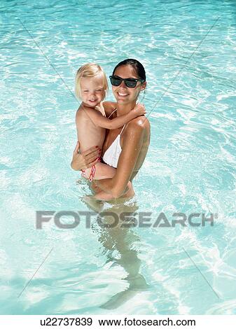 Stock Photo - Woman holding a young girl in a pool and smiling.. Fotosearch