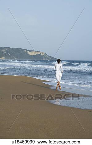 Stock Photo - Woman jogging away from camera on beach.. Fotosearch