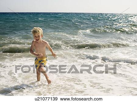 Young boy at the beach in shallow water smiling. View Large Photo Image Stock Photo - Young boy at the beach in shallow water smiling.. Fotosearch