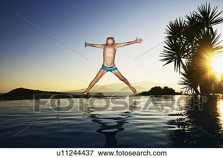 Young boy jumping into an infinity pool smiling. View Large Photo Image Stock Photo - Young boy jumping into an infinity pool smiling.. Fotosearch