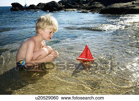 Young boy with a toy sailboat at the beach. View Large Photo Image Stock Image - Young boy with a toy sailboat at the beach.. Fotosearch
