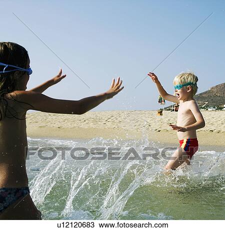 Stock Image - Young girl and young boy playing at the beach.. Fotosearch