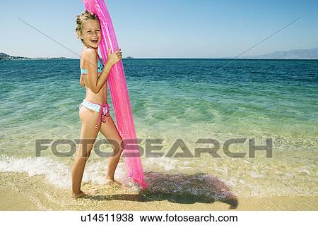 Stock Photo - Young girl holding up an inflatable raft at the beach smiling.. Fotosearch