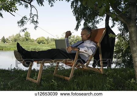 Businessman on deckchair with laptop by river. View Large Photo Image Stock Photo - Businessman on deckchair with laptop by river.. Fotosearch
