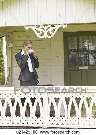 Stock Photo - Businesswoman by country cottage drinking coffee. Fotosearch