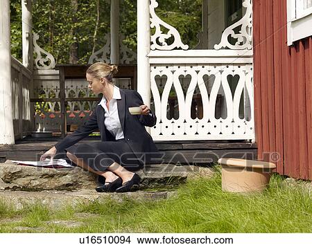 Picture - Businesswoman by country cottage with a newspaper. Fotosearch