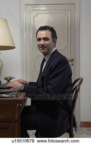 Stock Photo - Man using laptop in home office, portrait. Fotosearch