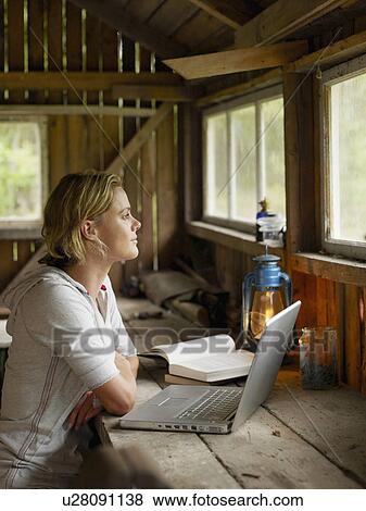 Woman with laptop and book sitting at table in cabin. View Large Photo Image Stock Photo - Woman with laptop and book sitting at table in cabin.. Fotosearch