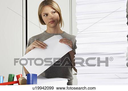 Stock Photo - Young woman working from home with huge pile of paper.. Fotosearch