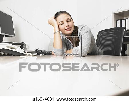Businesswomen sitting at her desk with a Newton's Cradle View Large Photo Image Stock Image - Businesswomen sitting at her desk with a Newton's Cradle. Fotosearch