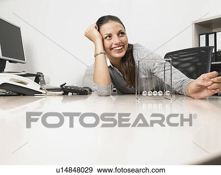Businesswomen sitting at her desk with a Newton's Cradle View Large Photo Image Stock Photo - Businesswomen sitting at her desk with a Newton's Cradle. Fotosearch
