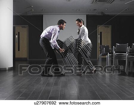 Man and woman moving stack of chairs in empty presentation room View Large Photo Image Stock Image - Man and woman moving stack of chairs in empty presentation room. Fotosearch