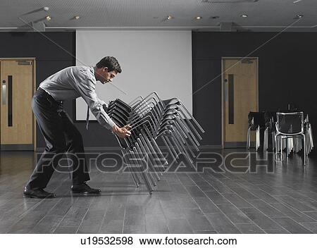 Man moving stack of chairs in empty presentation room View Large Photo Image Stock Photo - Man moving stack of chairs in empty presentation room. Fotosearch