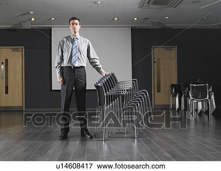 Man standing with stack of chairs in empty presentation room View Large Photo Image Stock Photo - Man standing with stack of chairs in empty presentation room. Fotosearch