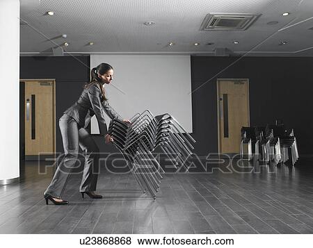Woman moving stack of chairs in empty presentation room View Large Photo Image Stock Photo - Woman moving stack of chairs in empty presentation room. Fotosearch
