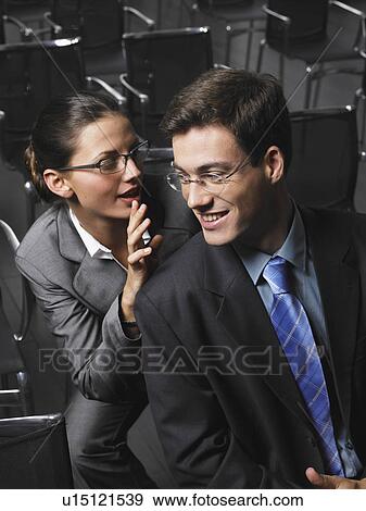 Stock Photo - Woman whispering to man sitting in auditorium. Fotosearch