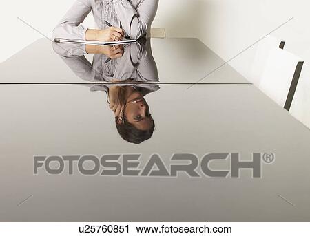 Stock Image - Young business woman at desk with reflections.. Fotosearch