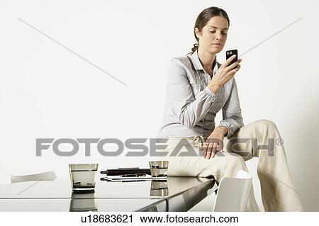 Young business woman seated on desk sending text message. View Large Photo Image Stock Image - Young business woman seated on desk sending text message.. Fotosearch