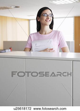 Young businesswoman holding file, standing in office, smiling View Large Photo Image Stock Image - Young businesswoman holding file, standing in office, smiling. Fotosearch