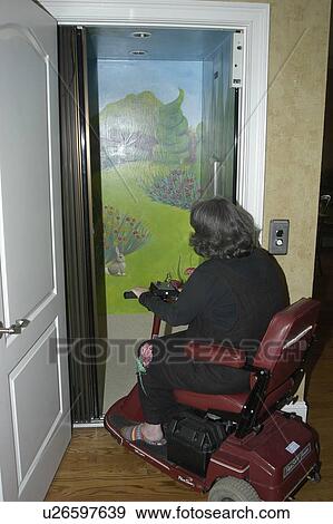 Stock Photo - A woman using a wheelchair enters a home elevator.. Fotosearch