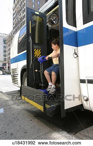 Stock Image - Boy with Muscular Dystrophy, utilizing a scooter/cart for mobility, exiting a city bus via a chair lift.. Fotosearch