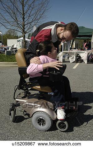 Stock Photo - Husband shares a joke with wife (wheelchair user) at outdoor event. Fotosearch