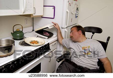 Stock Photograph - Man with a disability cooking his dinner in his kitchen, in his own apartment.. Fotosearch